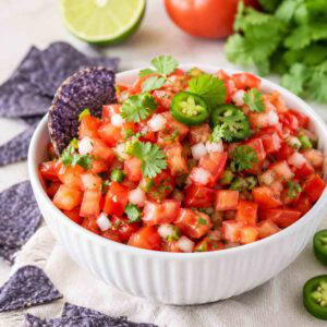 white bowl of pico de gallo topped with cilantro and blue chips.