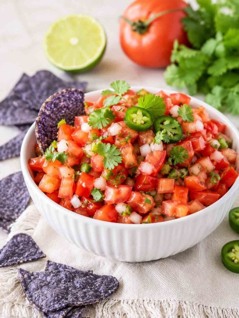 white bowl of pico de gallo topped with cilantro and blue chips.