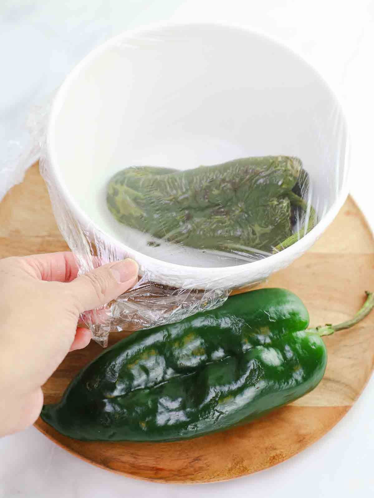 poblanos chili, one raw and one roasted and covered in a bowl.