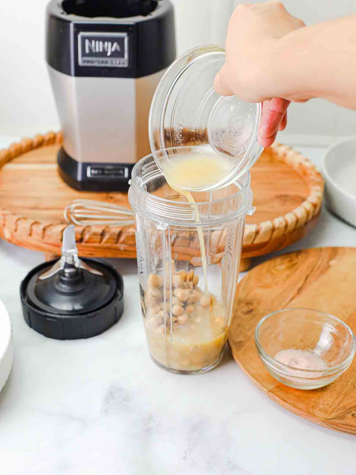 chickpeas with juice and spices being poured into a blender.