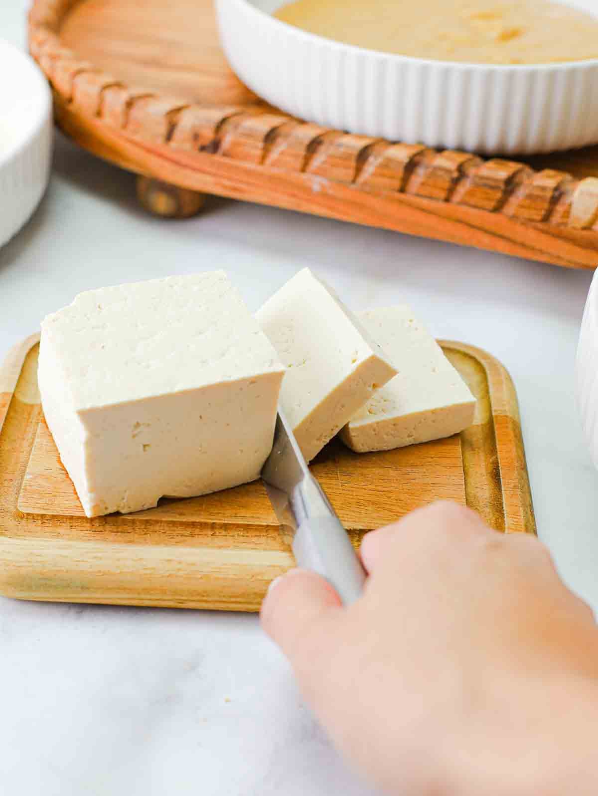 block of tofu being sliced on a cutting board.
