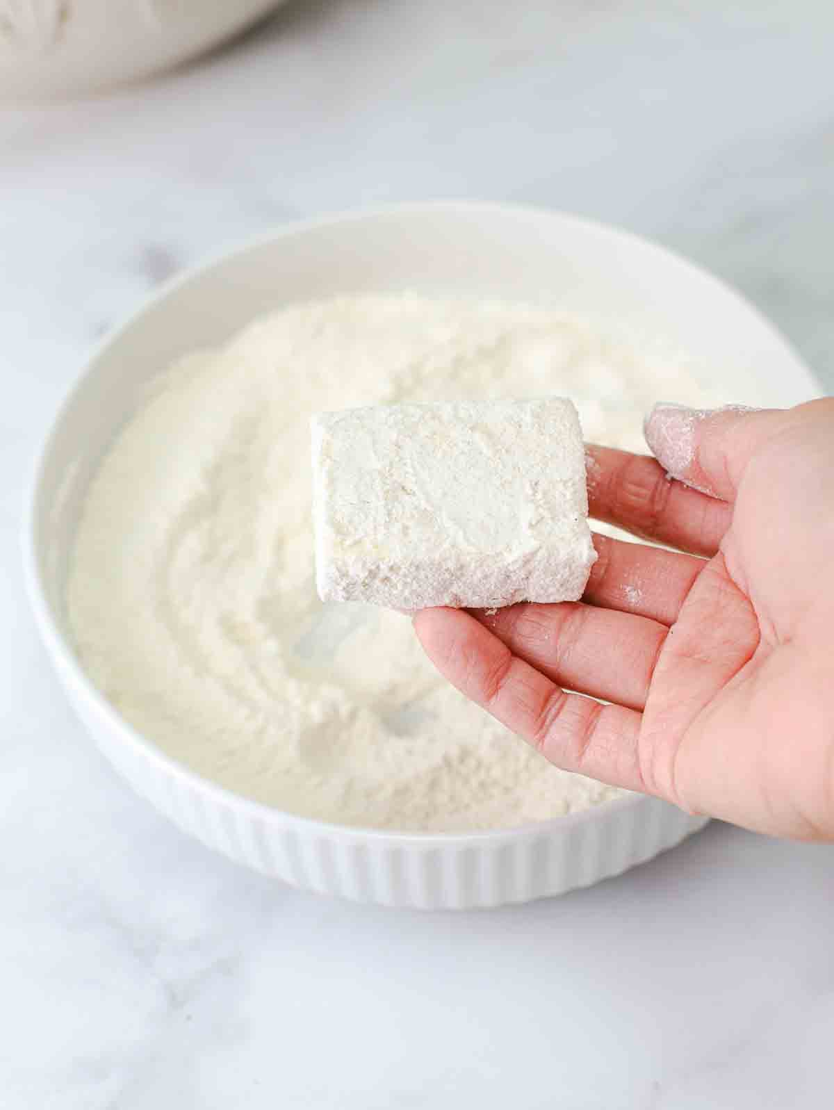 slice of tofu in a bowl of flour.