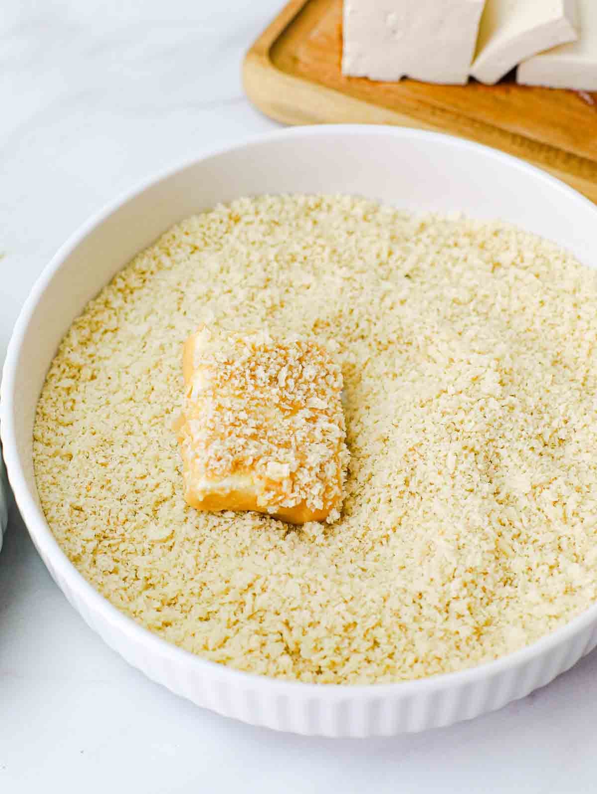 slice of tofu in a bowl of panko being breaded.