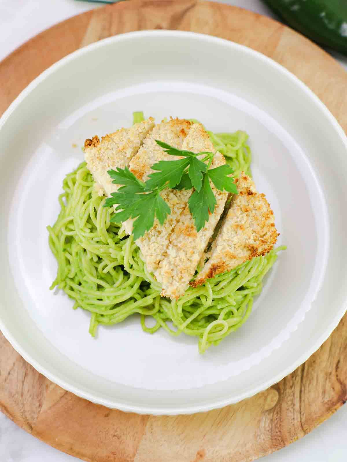 plate full of mexican green spaghetti with sliced crispy tofu on top.
