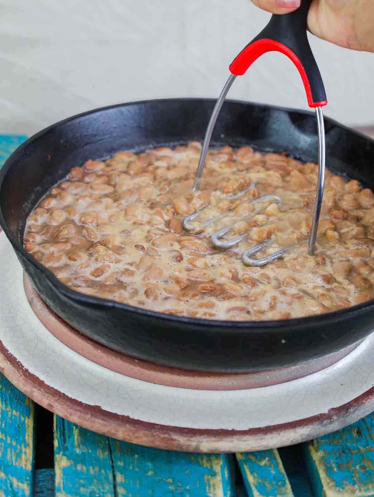 cast iron pan with refried pinto beans being mashed.