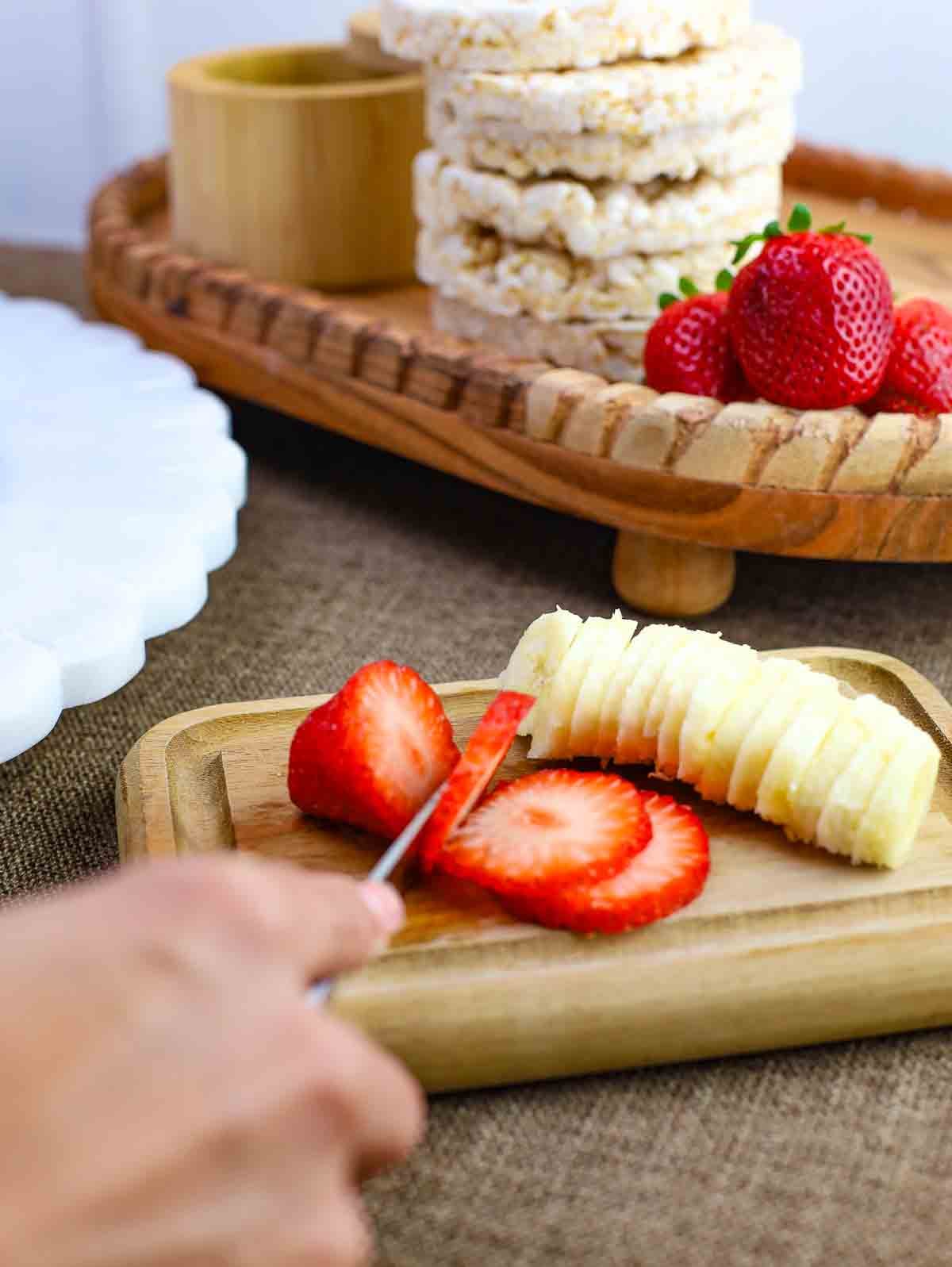 strawberries and bananas being sliced on a wooden cutting board.