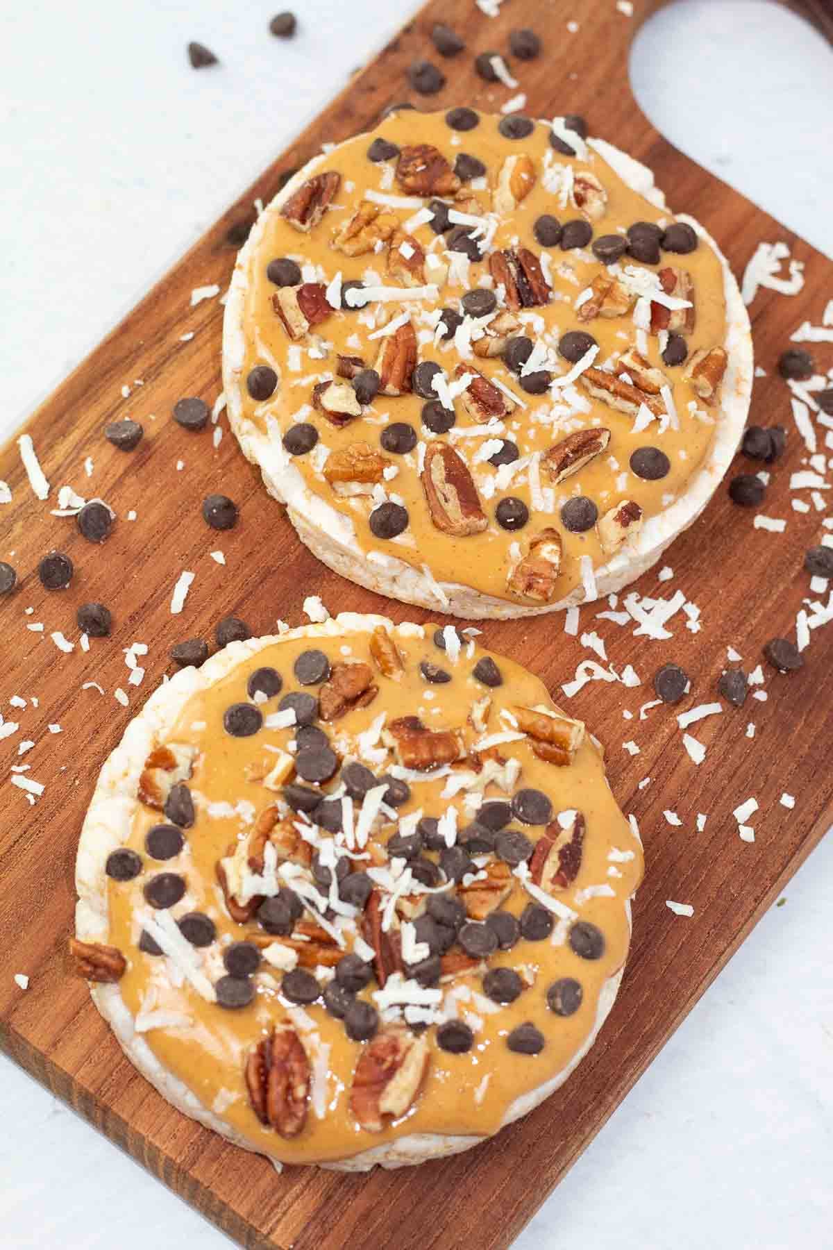 close up of peanut butter and chocolate chip rice cake desserts on a wooden board topped with shredded coconut.
