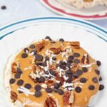 peanut butter, chocolate chips, pecans, and shredded coconut on a rice cake on a white plate.