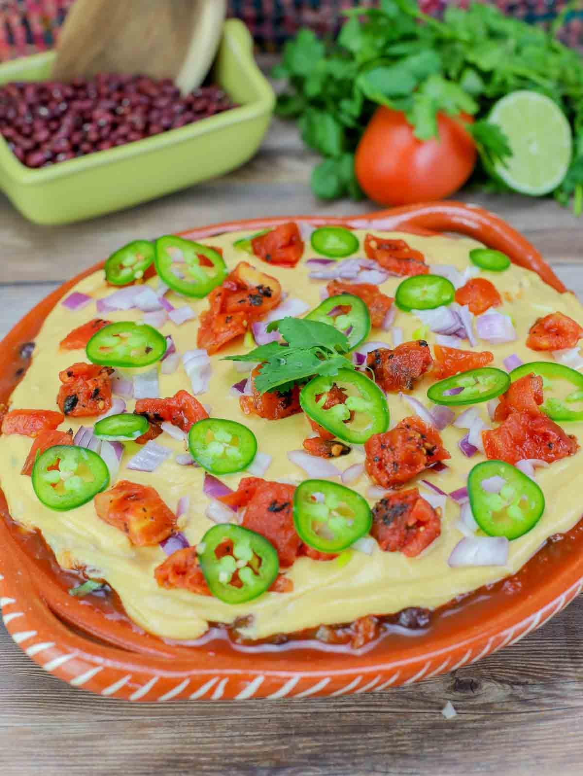big dish of 7-layer dip topped with jalepenos, tomatoes, and purple onion.