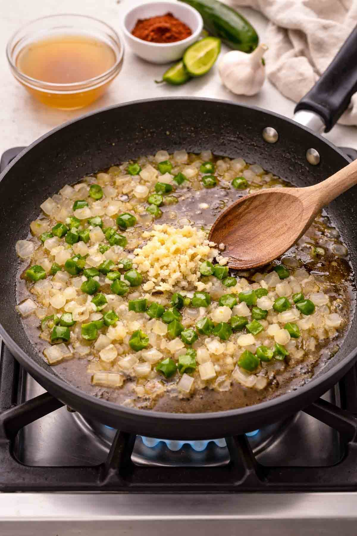 skillet with onions, garlic, and jalepenos being sauteed on a stovetop.