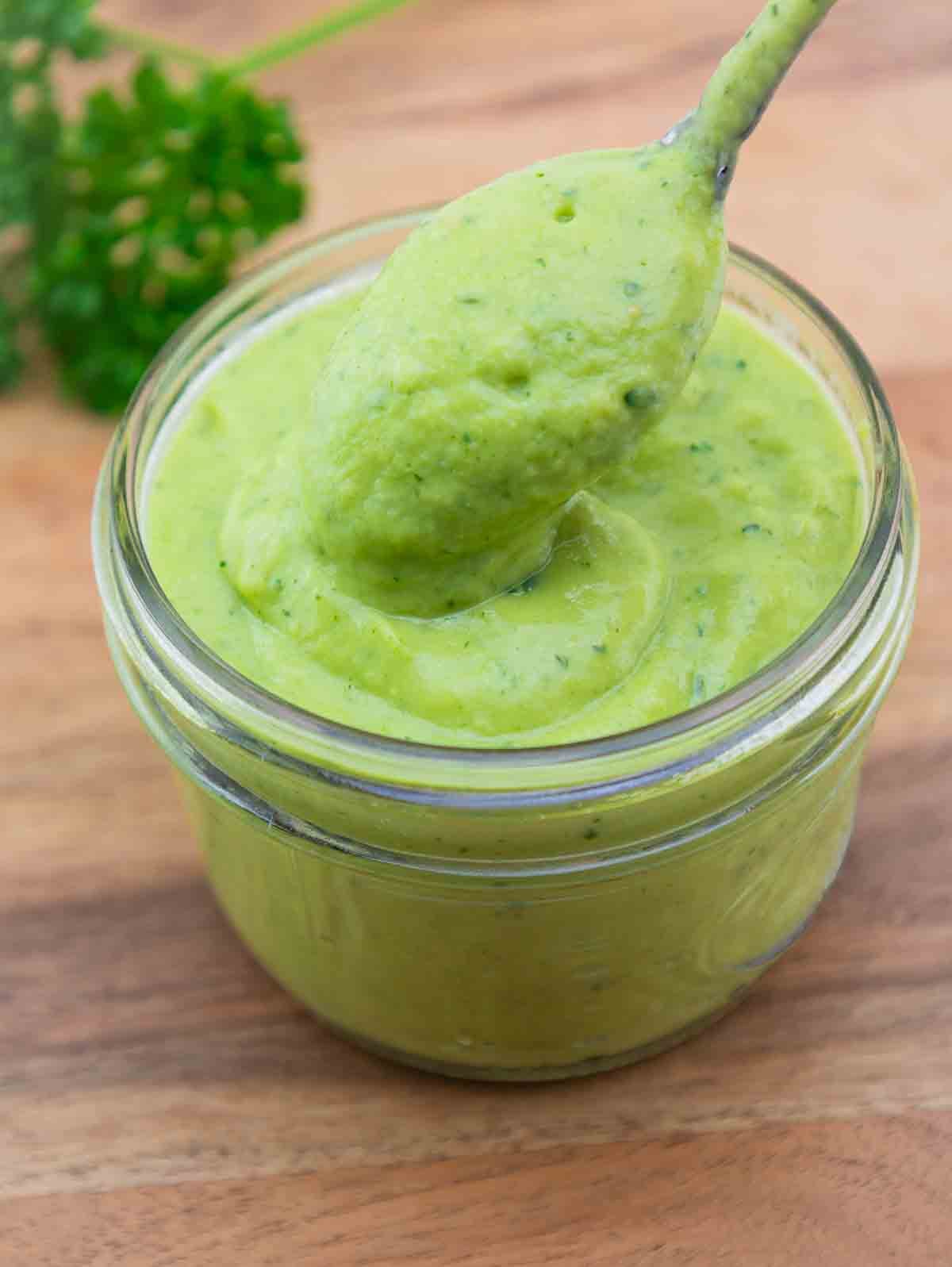 spoonfull of avocado salad dressing over a glass mason jar.