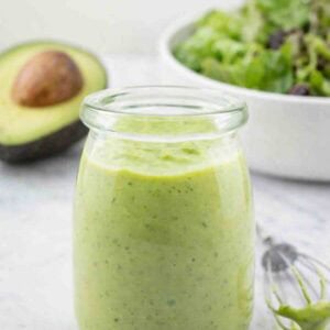 creamy avocado dressing in a glass jar with a small whisk beside.