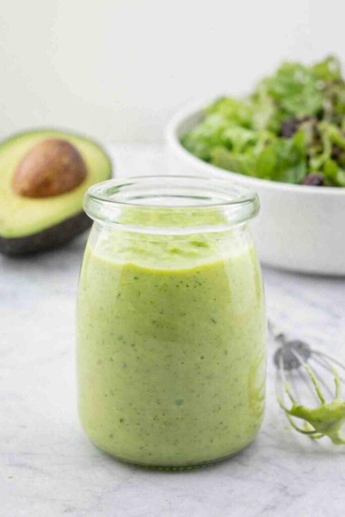 creamy avocado dressing in a glass jar with a small whisk beside.