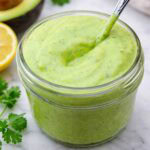 avocado cilantro dressing in a small jar with a spoon.