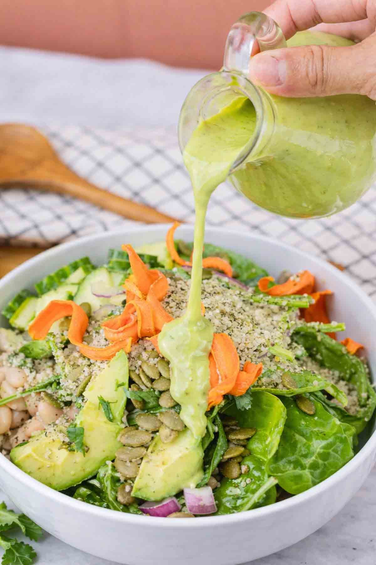 green salad in a bowl with avocado dressing being poured over the top.