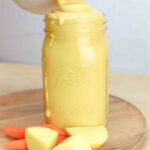 vegan cheese sauce in a mason jar with potato and carrot slices beside the jar.