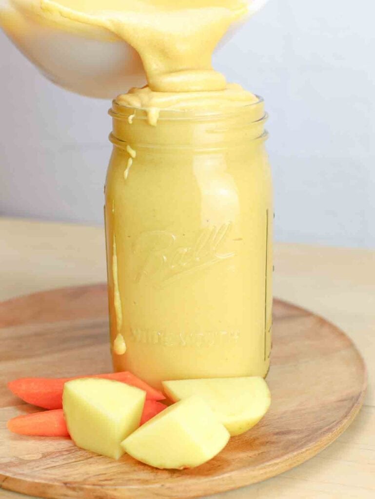 vegan cheese sauce in a mason jar with potato and carrot slices beside the jar.