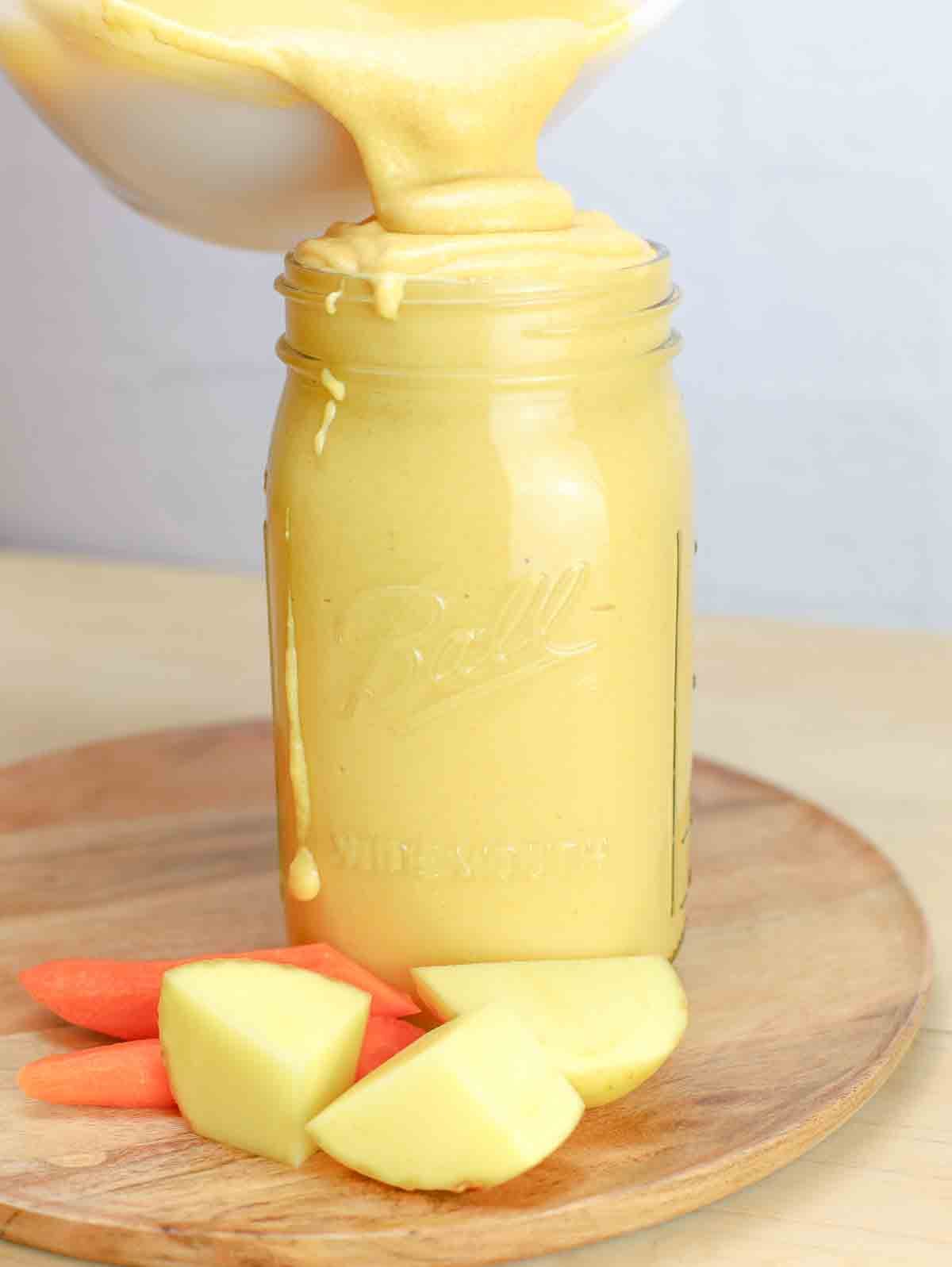 vegan cheese sauce in a mason jar with potato and carrot slices beside the jar.