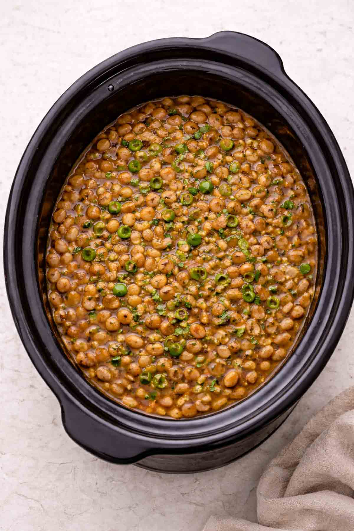 slow cooker full of seasoned cooked pinto beans.