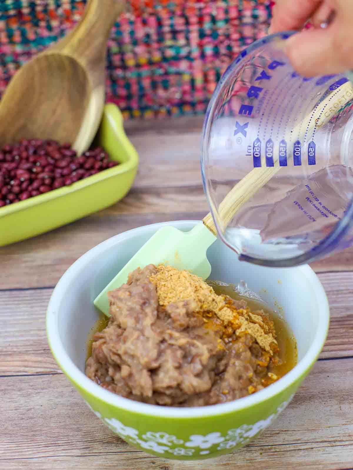 refried beans in a bowl with taco seasoning being stirred.