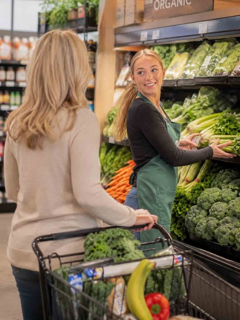 women in grocery store produce section smiling and talking.