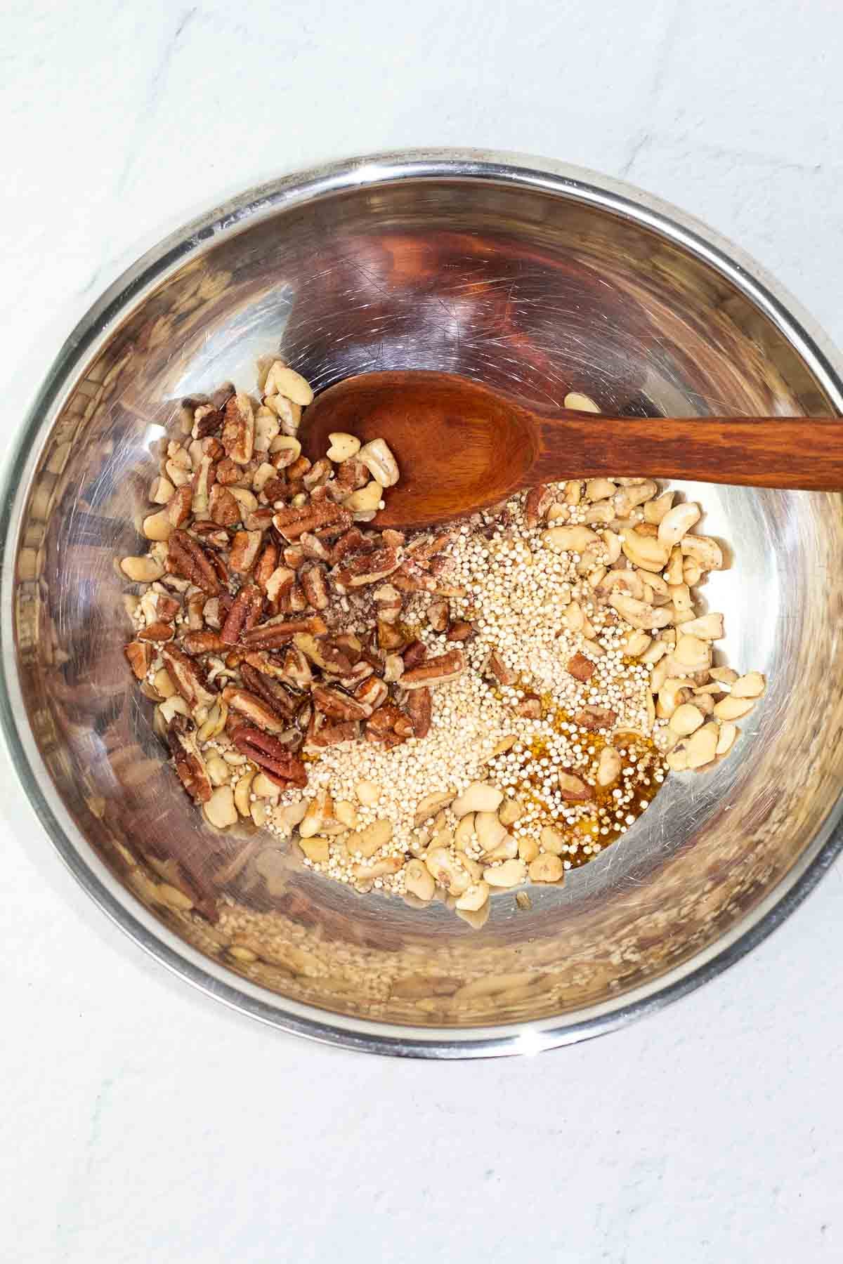 quinoa, cashews, pecans, and maple syrup in mixing bowl with spoon.