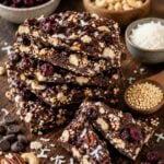 quinoa chocolate bark pieces stacked on a cutting board with ingredients in bowls surrounding.