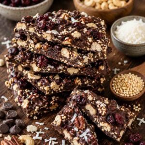 quinoa chocolate bark pieces stacked on a cutting board with ingredients in bowls surrounding.