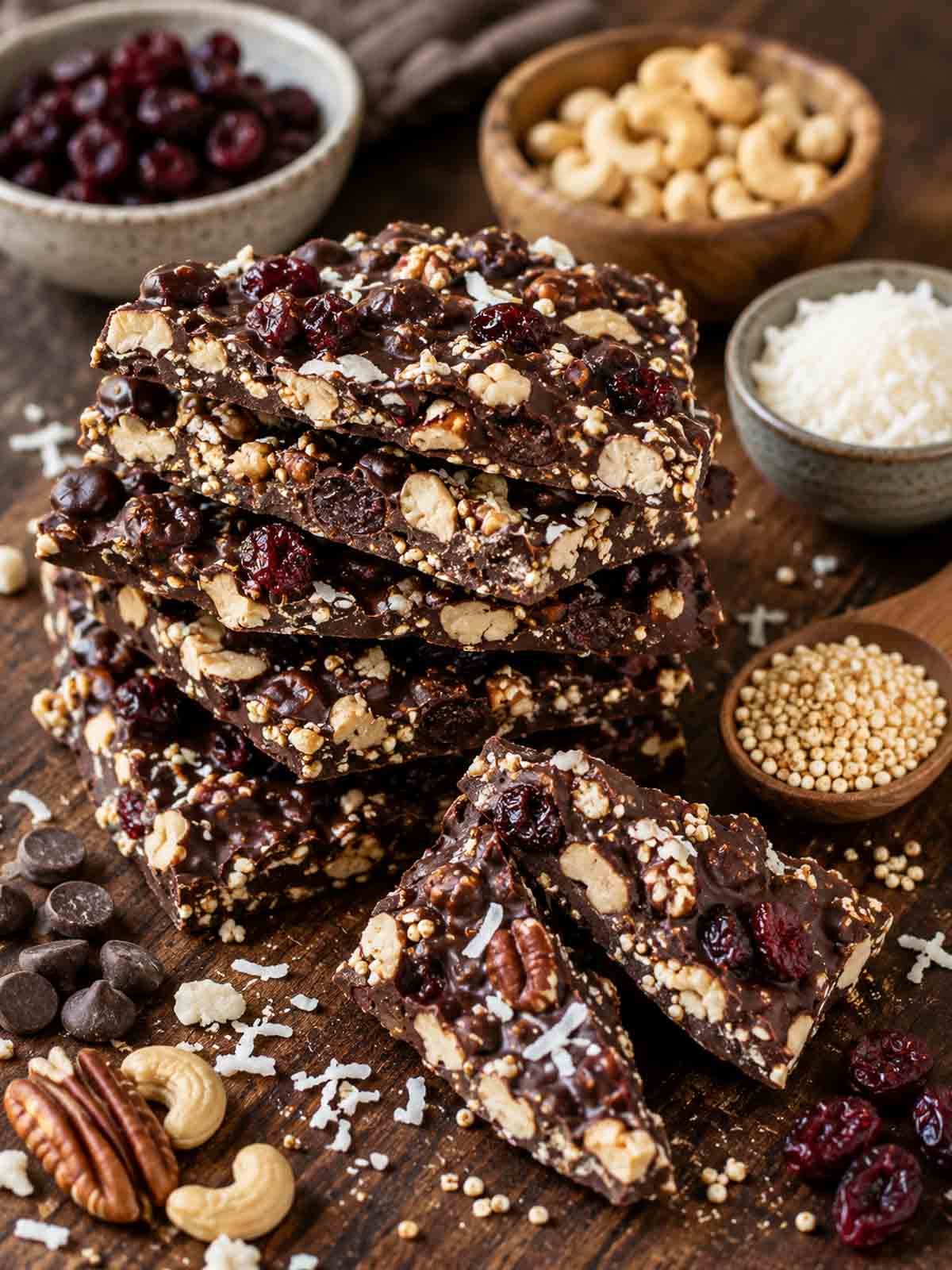quinoa chocolate bark pieces stacked on a cutting board with ingredients in bowls surrounding.