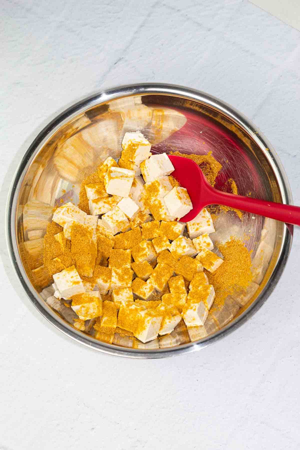 cubes of tofu with seasoning in a bowl with a spoon being stirred.