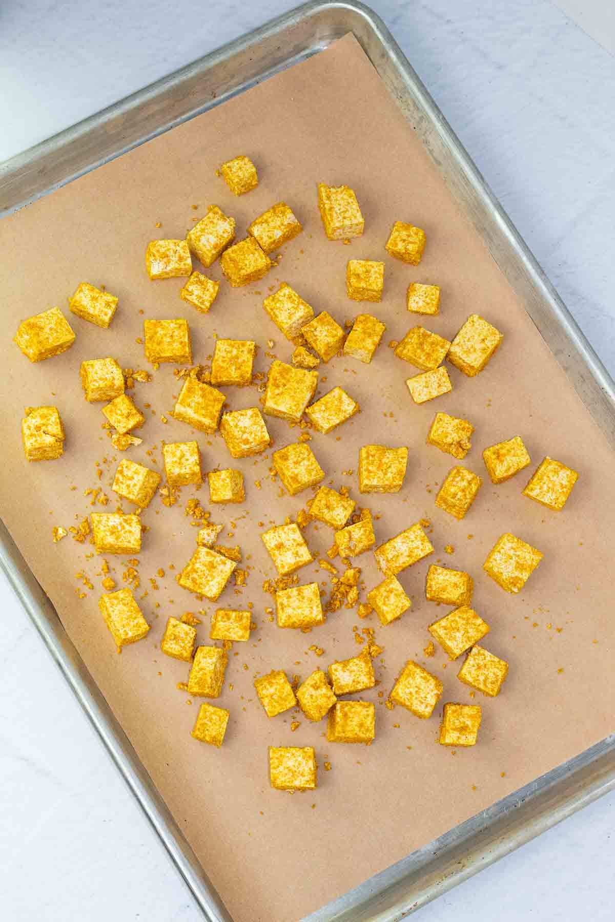 baking sheet lined with parchment paper and cubes of seasoned tofu.