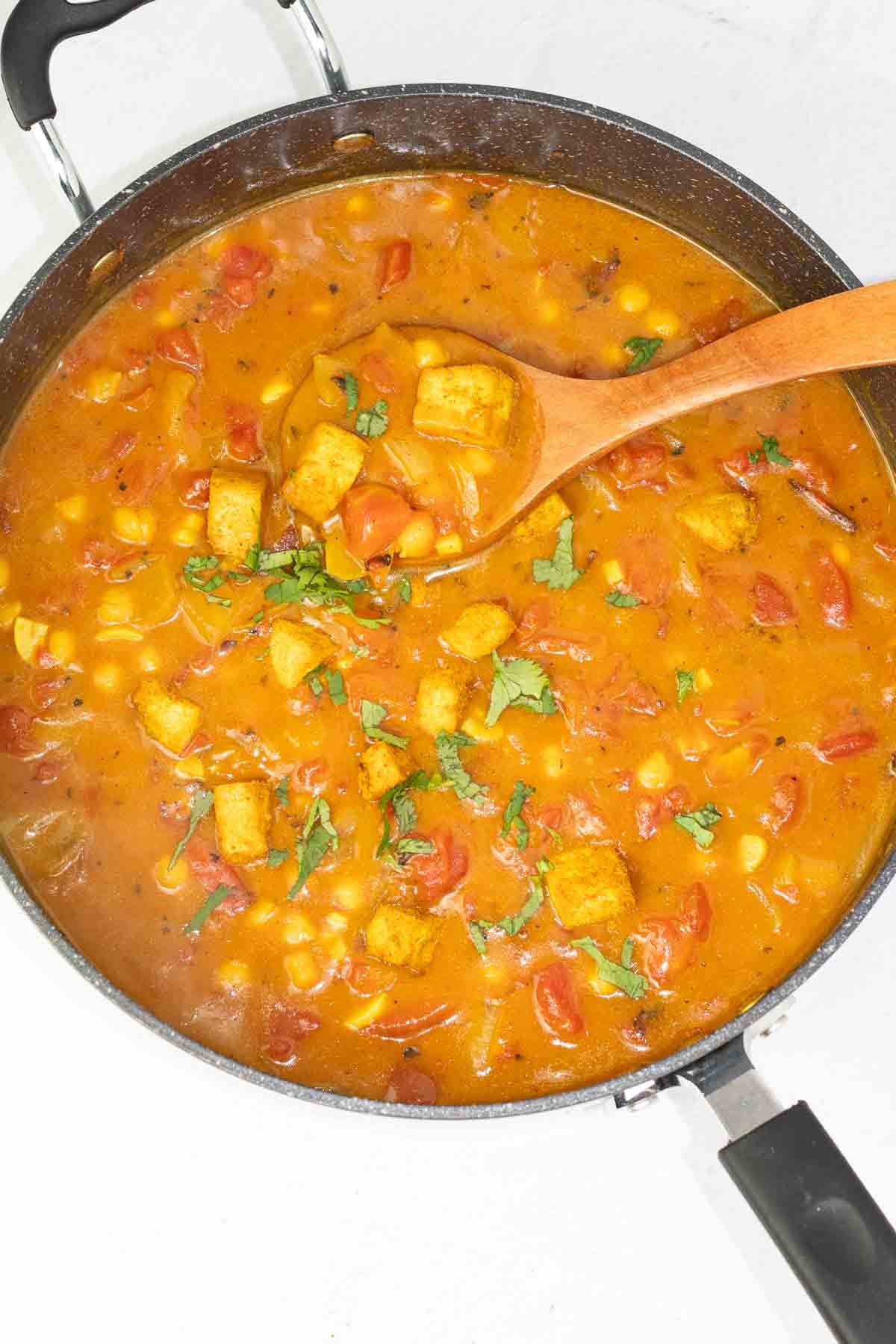 finished photo of curry tofu in a pan with a wooden spoon.