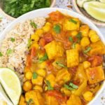 white bowl filled with tofu curry and brown rice with a slice of lime.