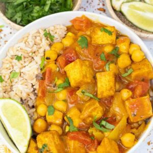 white bowl filled with tofu curry and brown rice with a slice of lime.