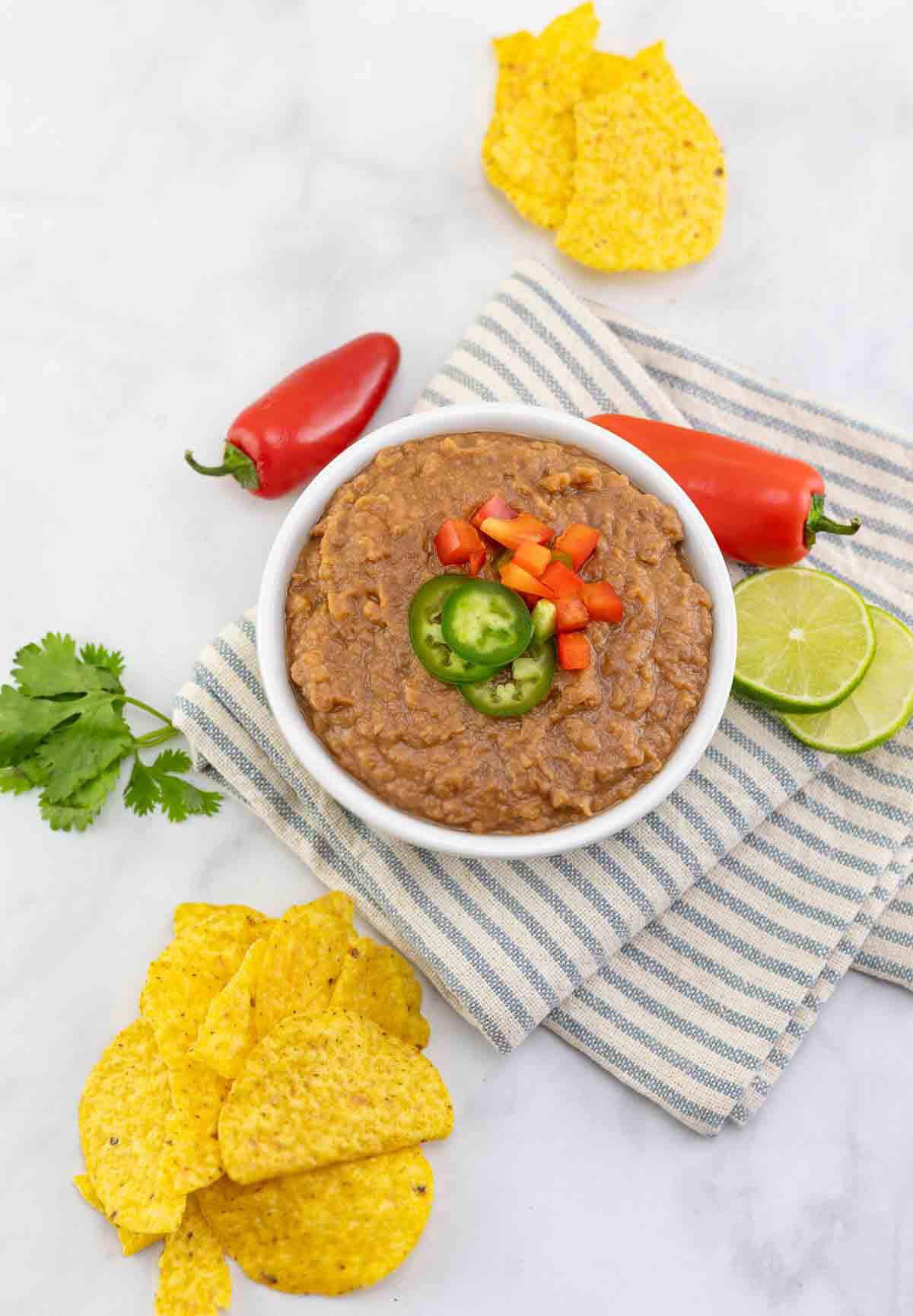 overhead shot of bean dip on white countertop with peppers, lime slices, and corn chips.