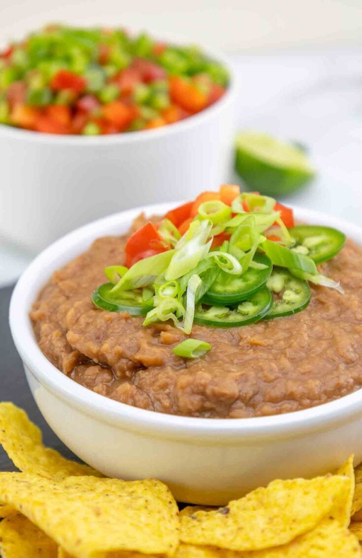 bean dip in a white bowl topped with chopped green onions and jalapenos.