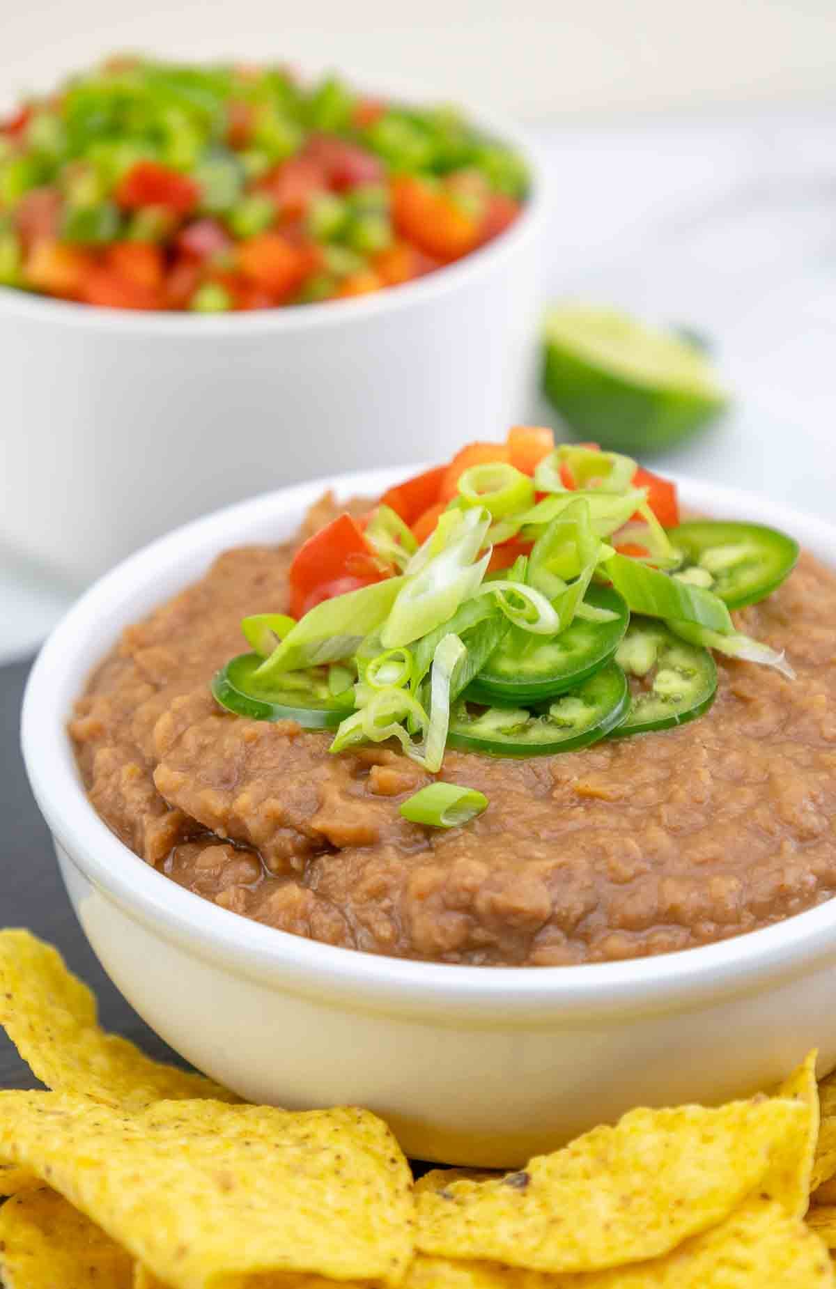 bean dip in a white bowl topped with chopped green onions and jalapenos.
