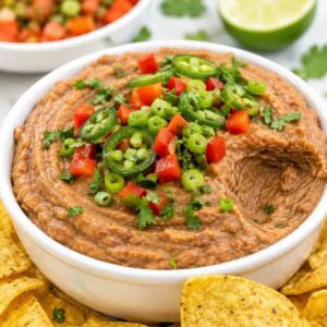 easy black bean dip in a white bowl topped with cilantro, peppers, jalapeno, and one scoop missing.