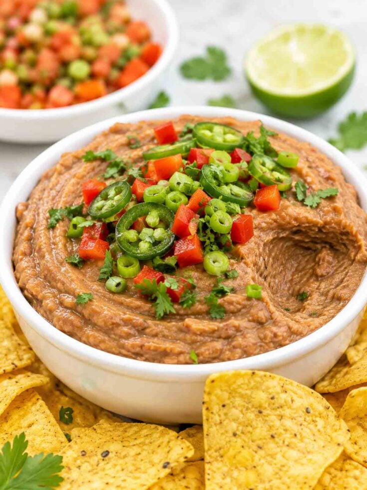 easy black bean dip in a white bowl topped with cilantro, peppers, jalapeno, and one scoop missing.