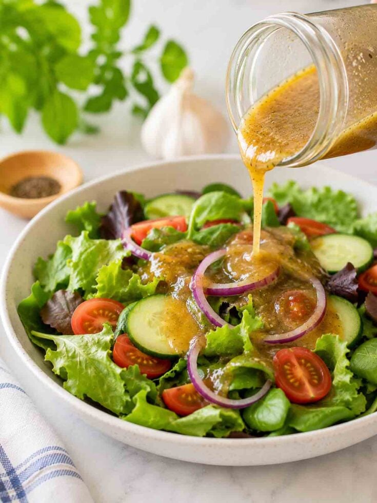 oil-free maple dijon dressing being poured over a garden salad.