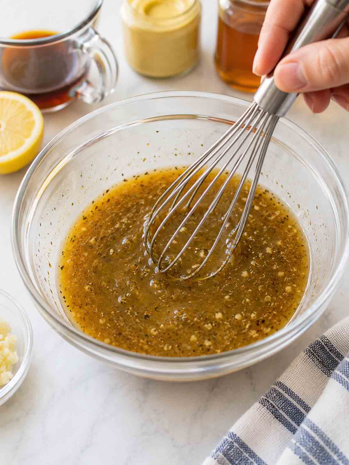maple dijon dressing being whisked together in glass bow.