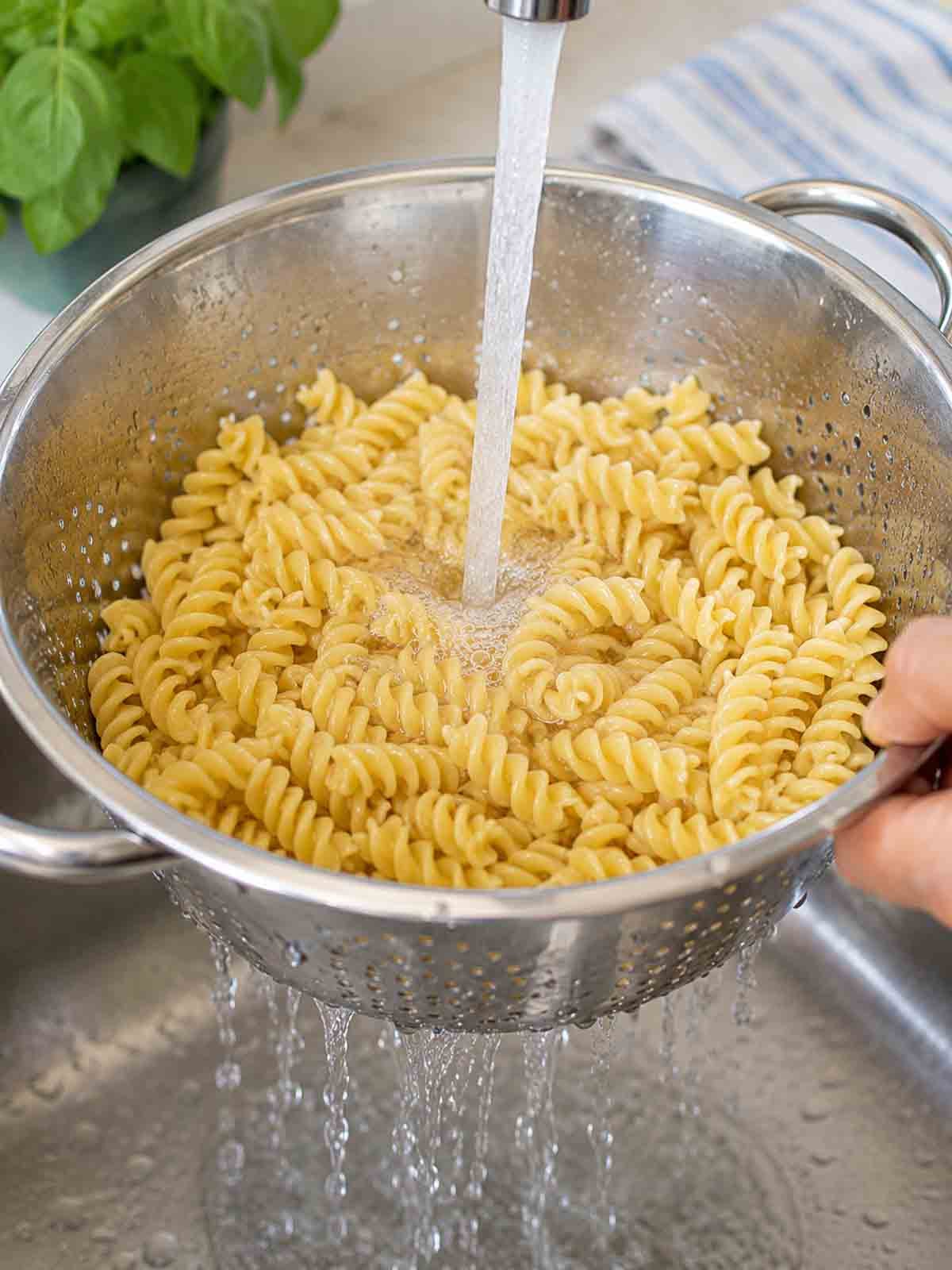 spiral pasta being rinsed in colander in sink.