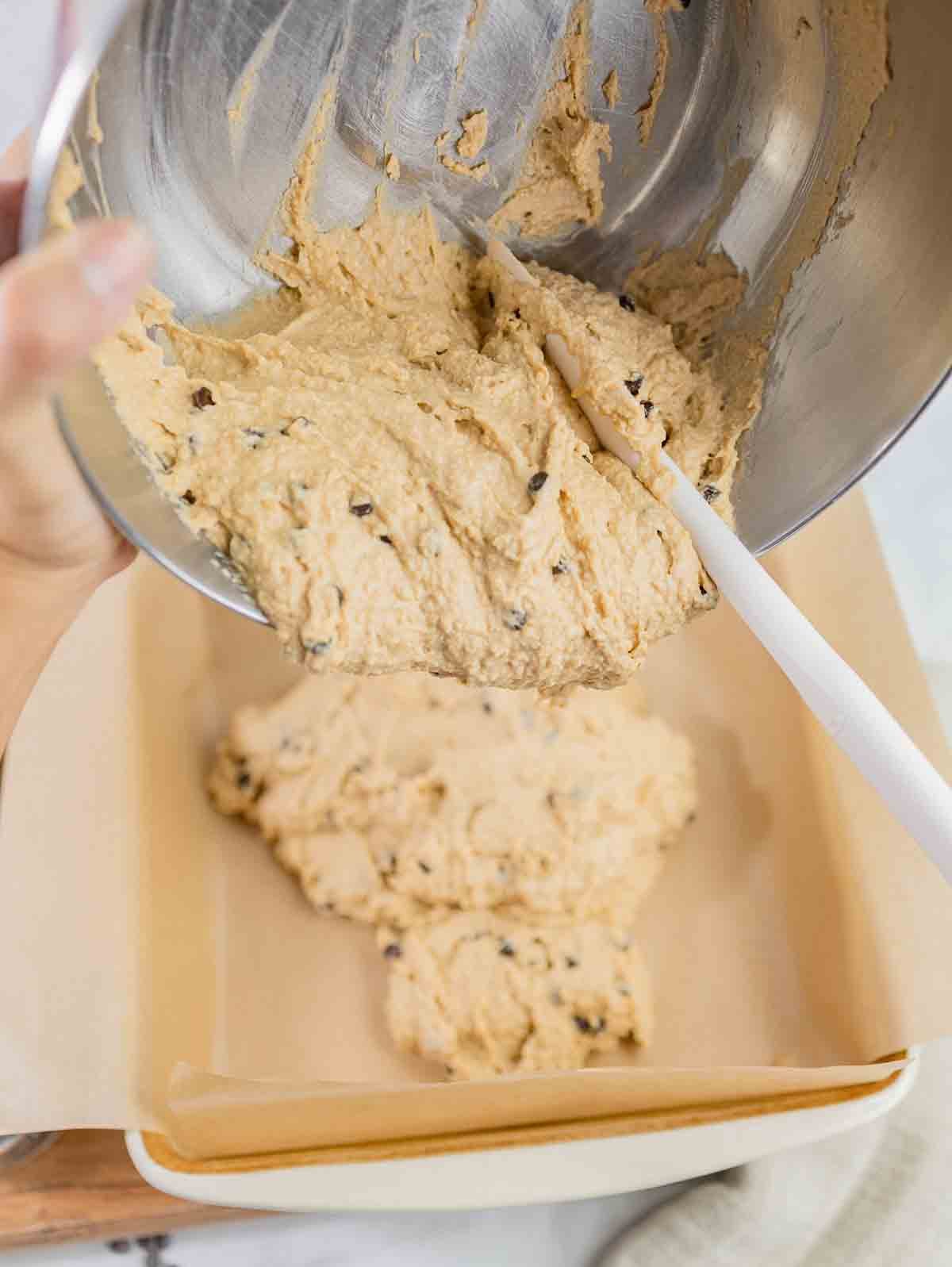chickpea blondie batter being poured from a mixing bowl into a baking dish.