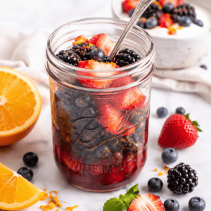 pint mason jar filled with macerated strawberries, blueberries, and blackberries with spoon in jar.