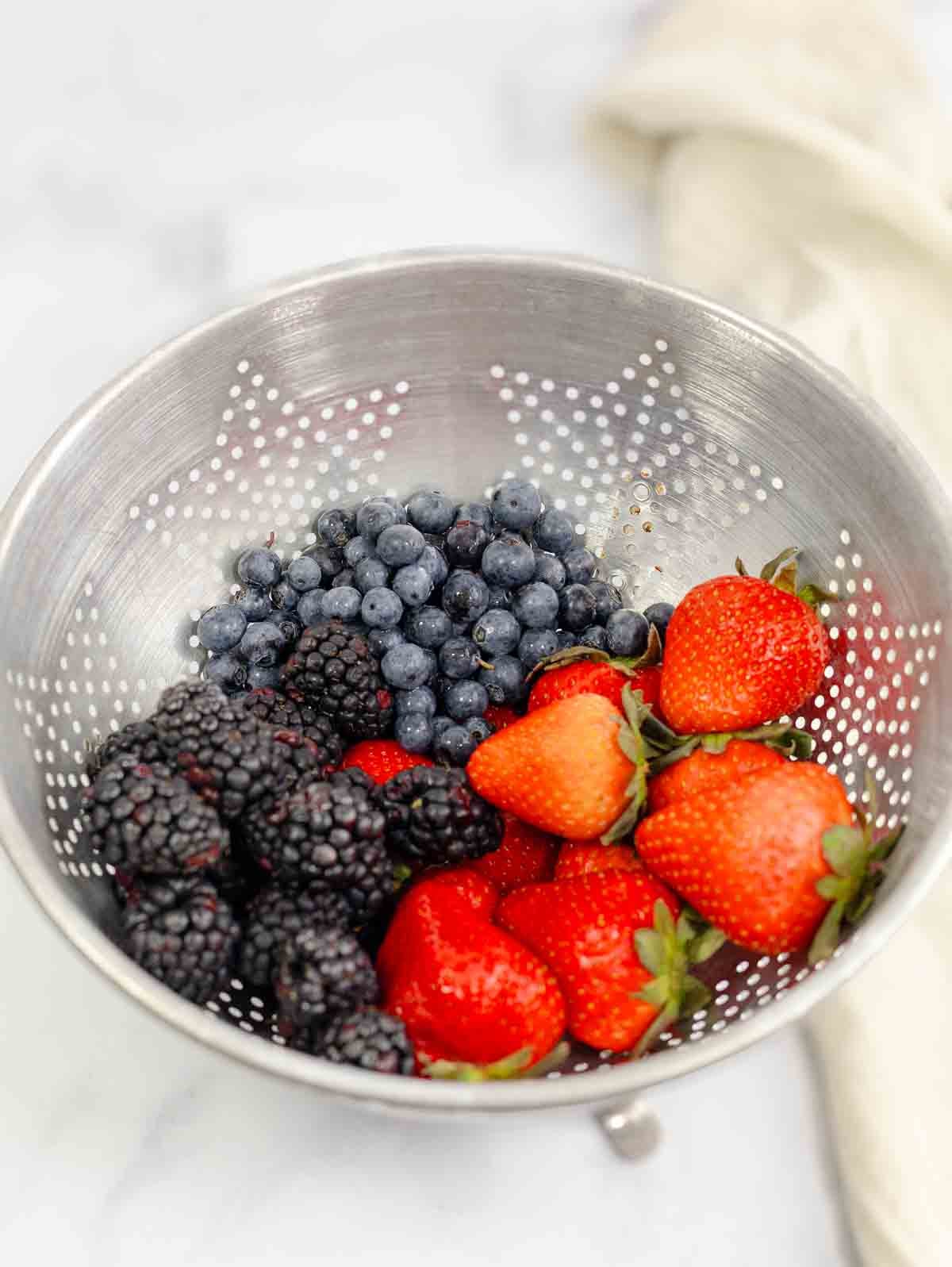 steel colander filled with strawberries, blackberries, and blueberries.