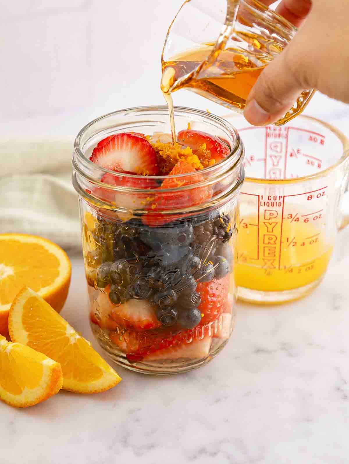 maple syrup being poured into a jar of macerated berries.