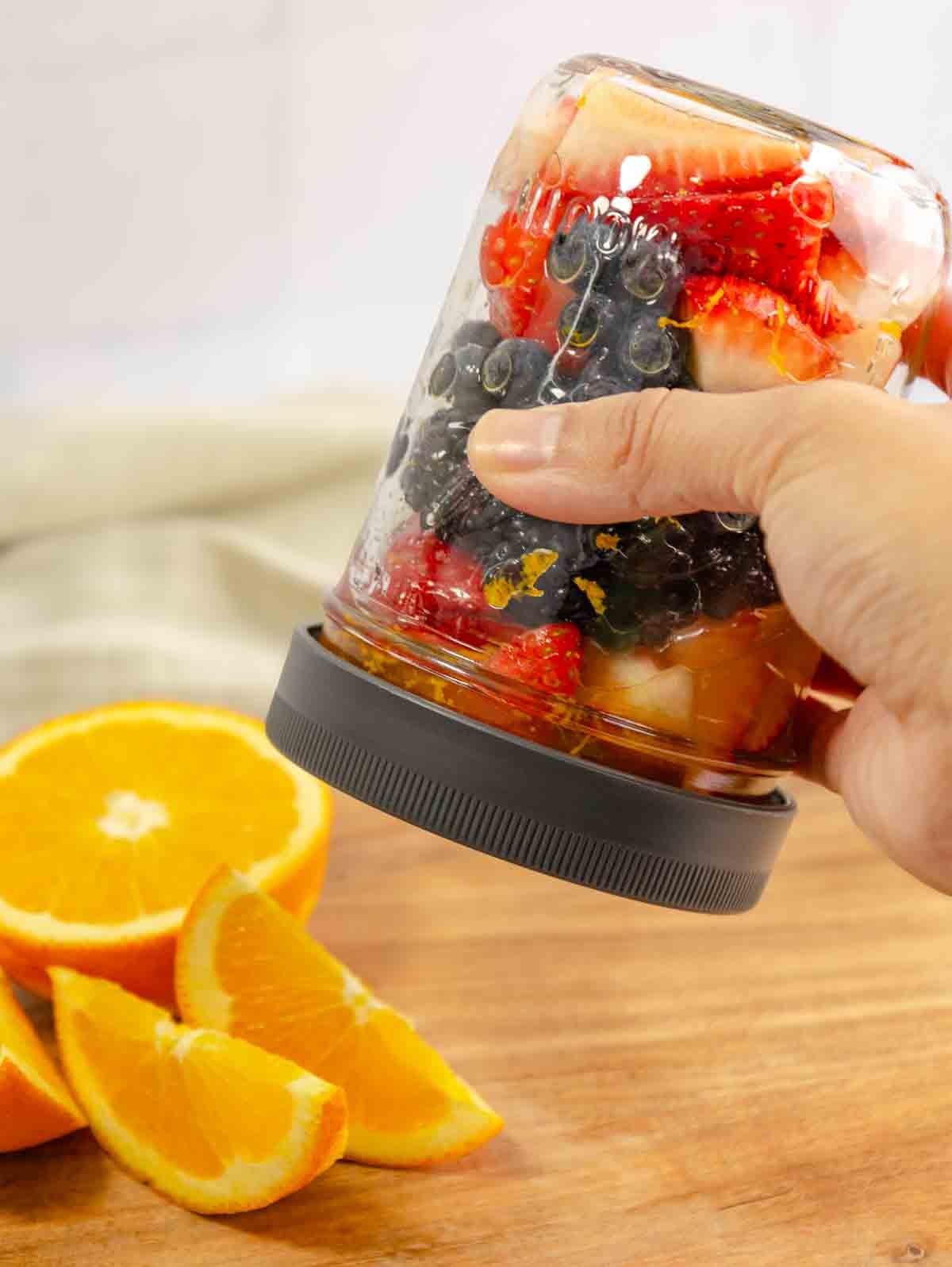 person shaking a jar of maceratedberries with lid on.