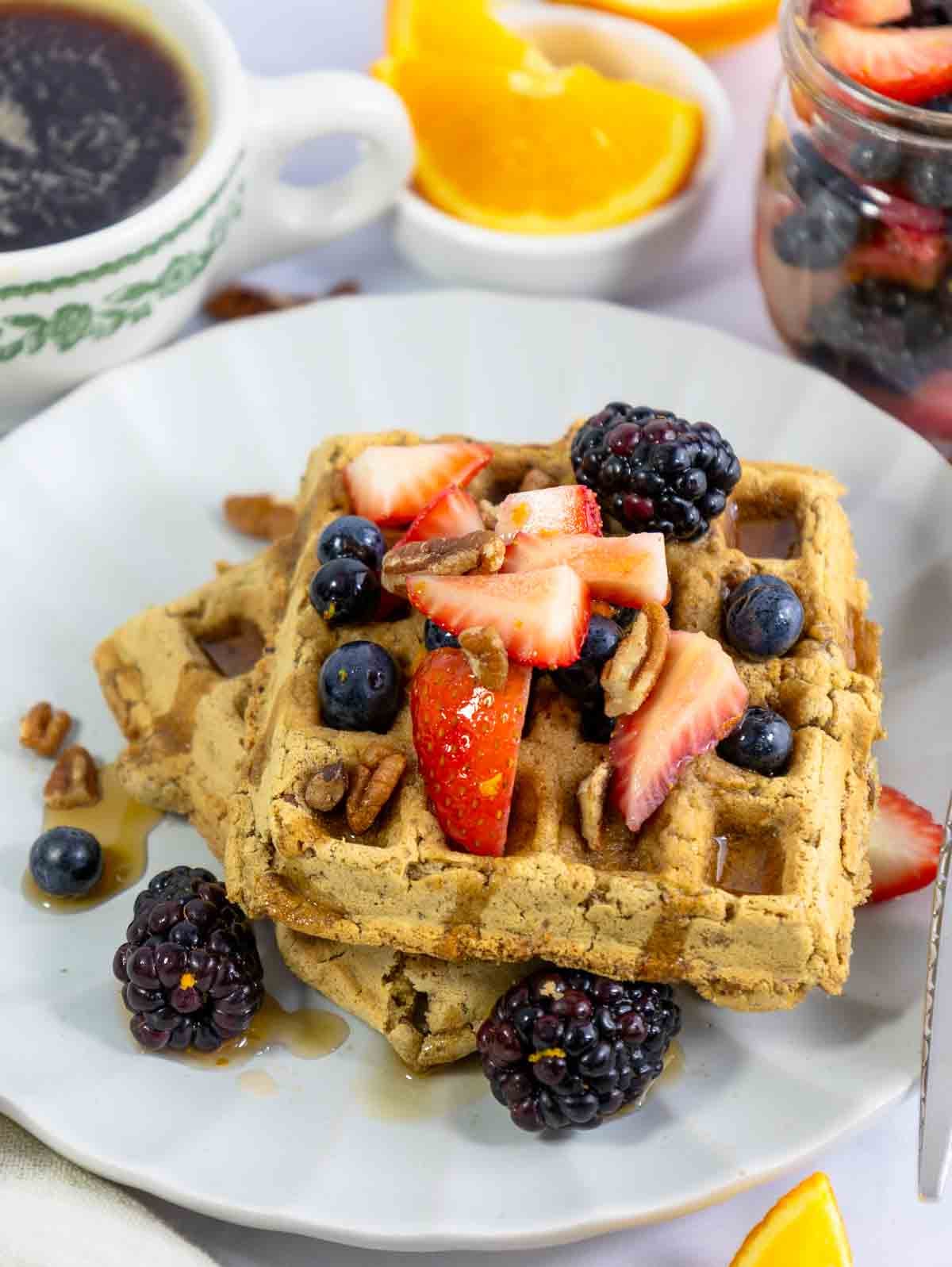 two vegan pecan waffles on a white plate topped with berries.