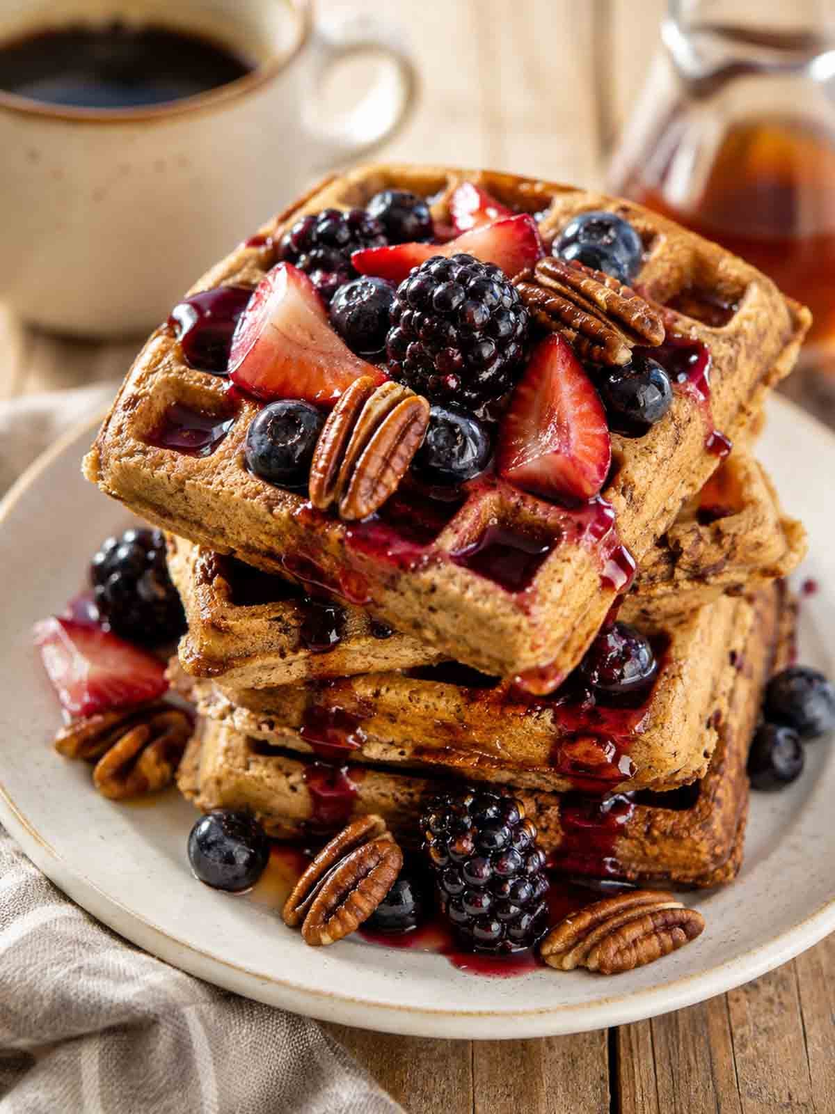 stack of pecan waffles topped with pecan halves, strawberries, blackberries, and blueberries.
