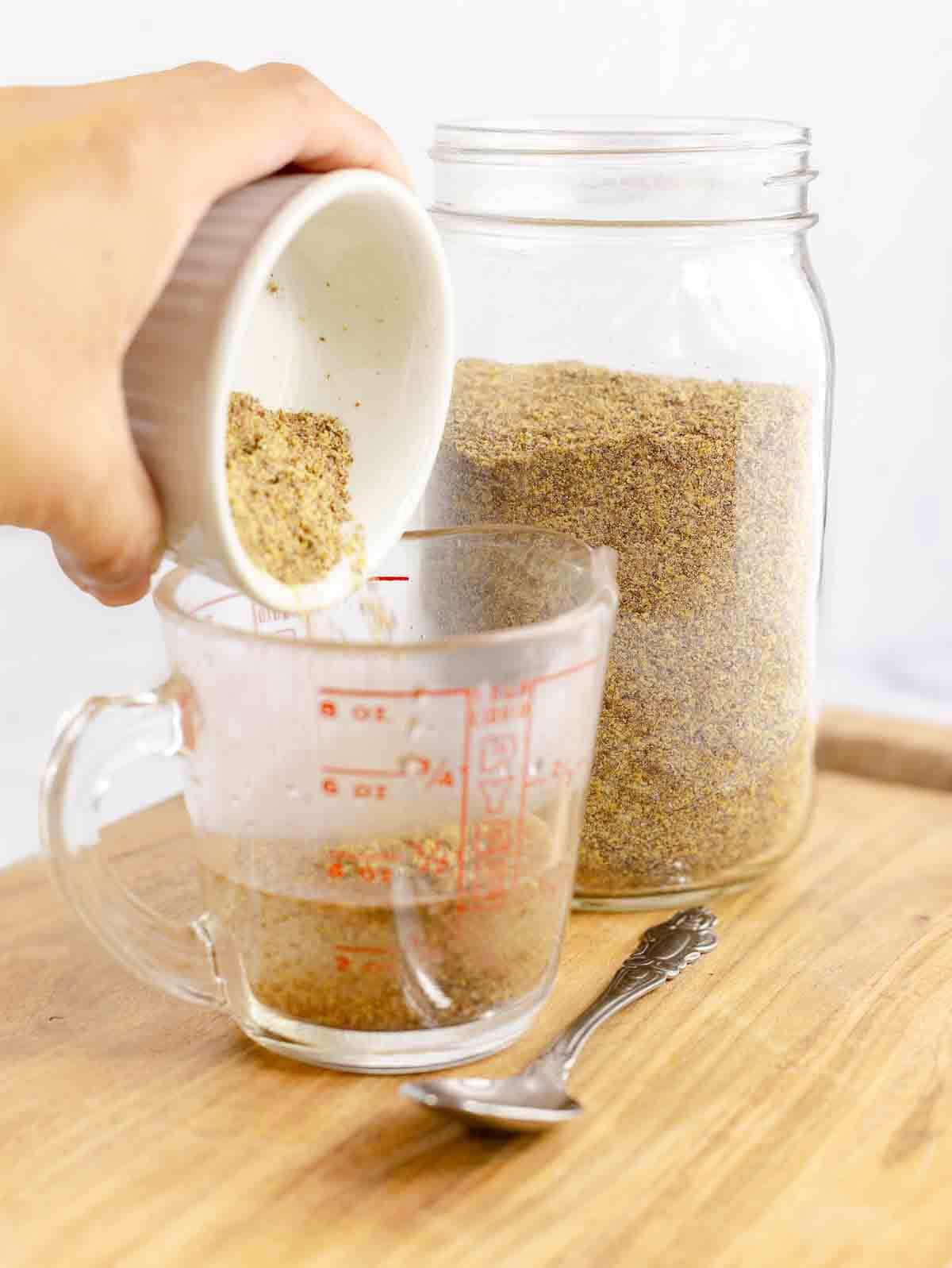 flaxmeal being added to a clear measuring cup with water.